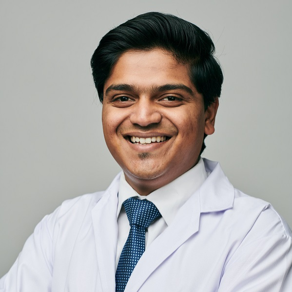 Male dentist Dr. Sandesh Jain smiling confidently in white coat at dental clinic