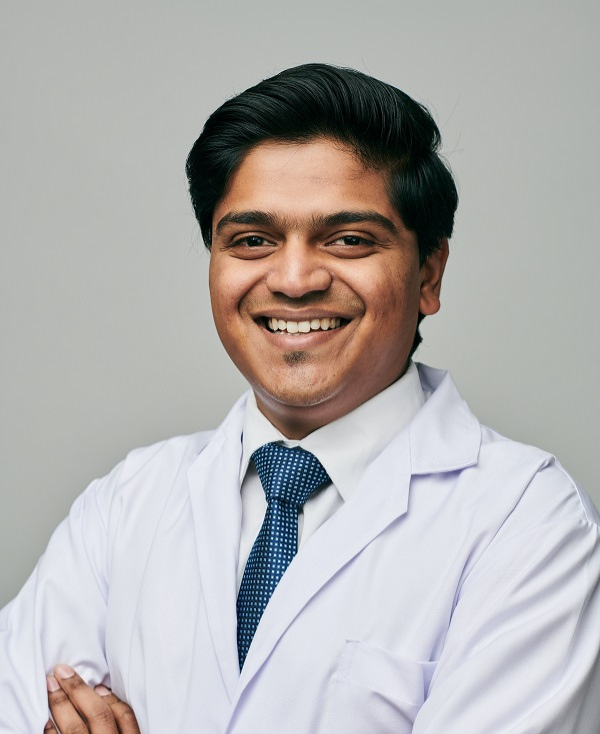 Male dentist Dr. Sandesh Jain smiling confidently in white coat at dental clinic